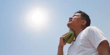 man in the sun holding wet cloth to neck