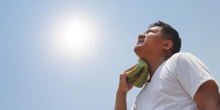 man in the sun holding wet cloth to neck