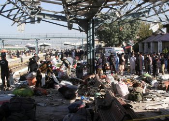 police officers and people gather at the site amid the debris after a bomb blast at a railway station in quetta