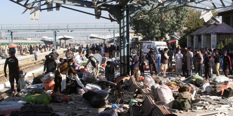 police officers and people gather at the site amid the debris after a bomb blast at a railway station in quetta